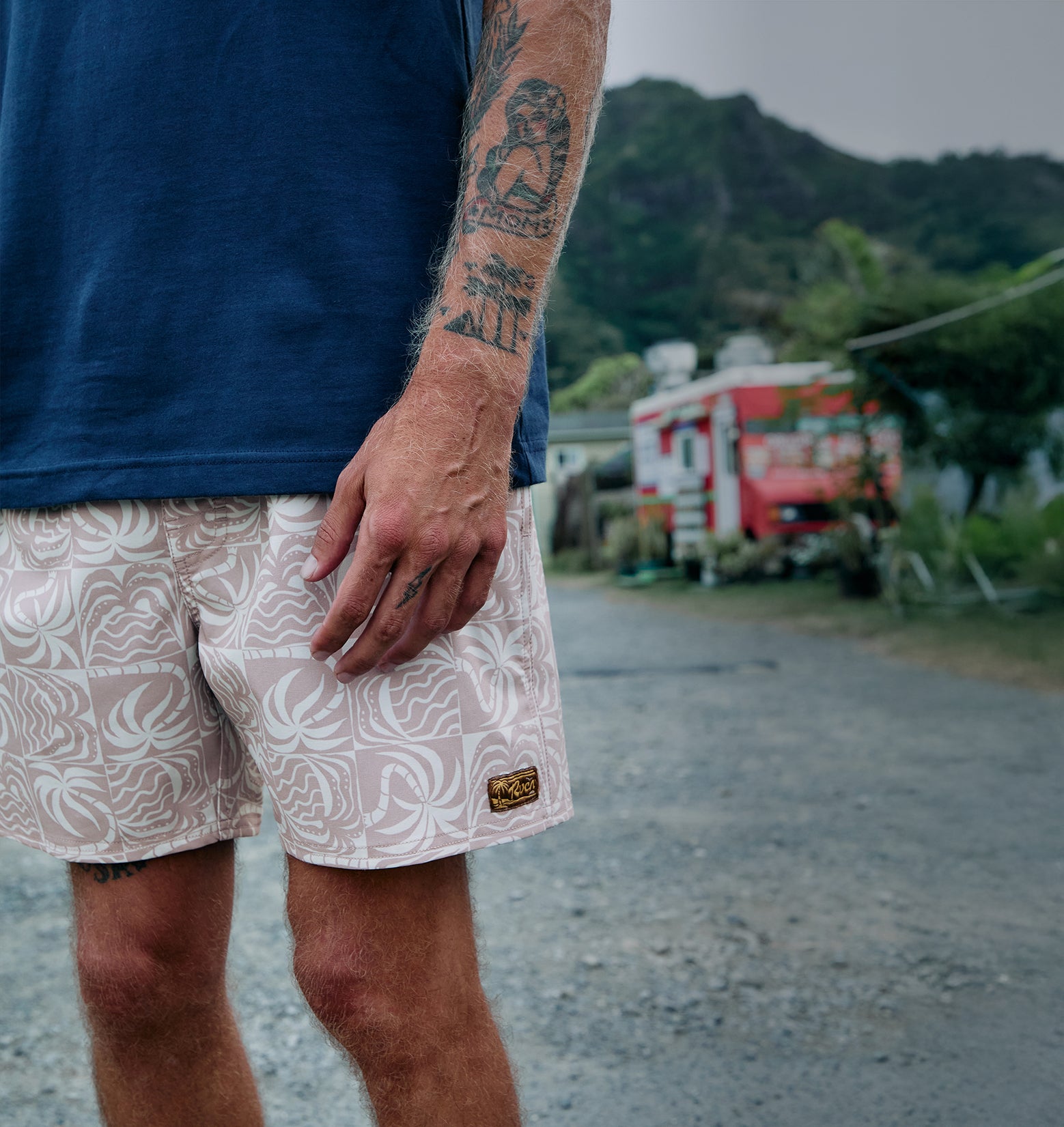 Person wearing a blue shirt and patterned shorts with a blurred background of a road and greenery.