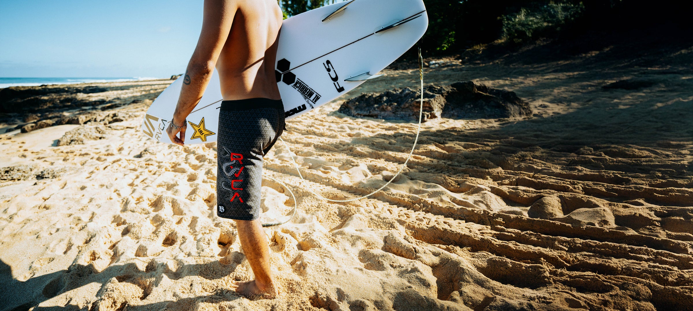 Person holding a surfboard on a sandy beach with clear skies