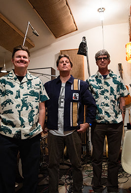 Three men wearing matching patterned shirts in a room with musical instruments.