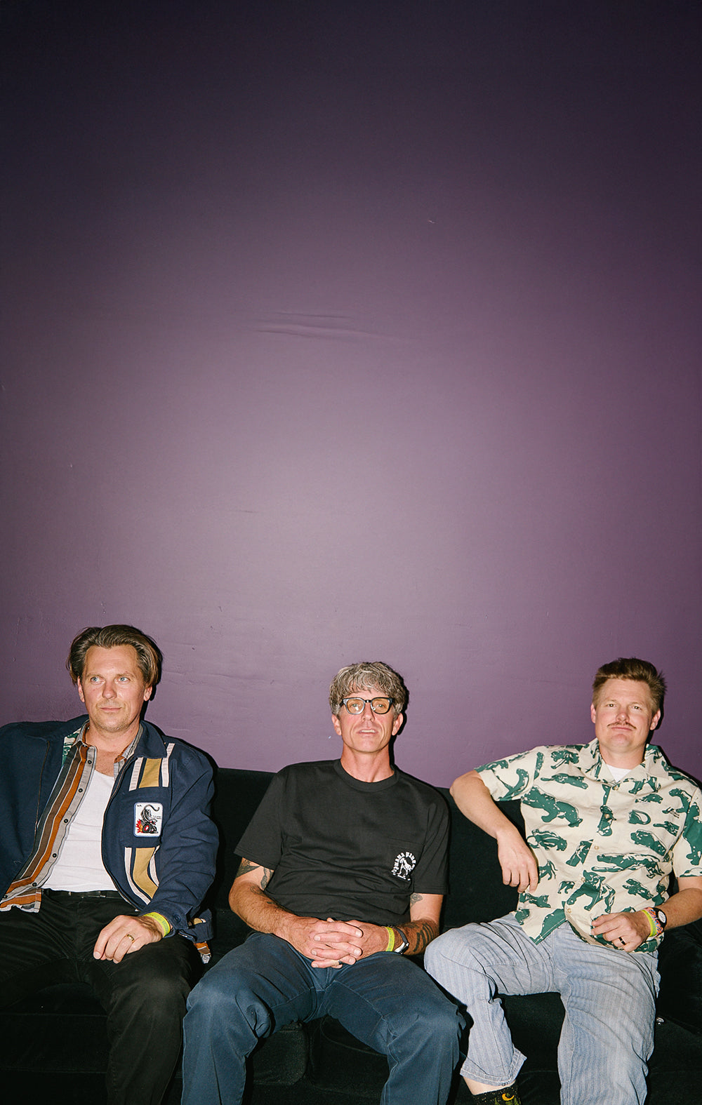 Three men sitting on a couch against a purple wall