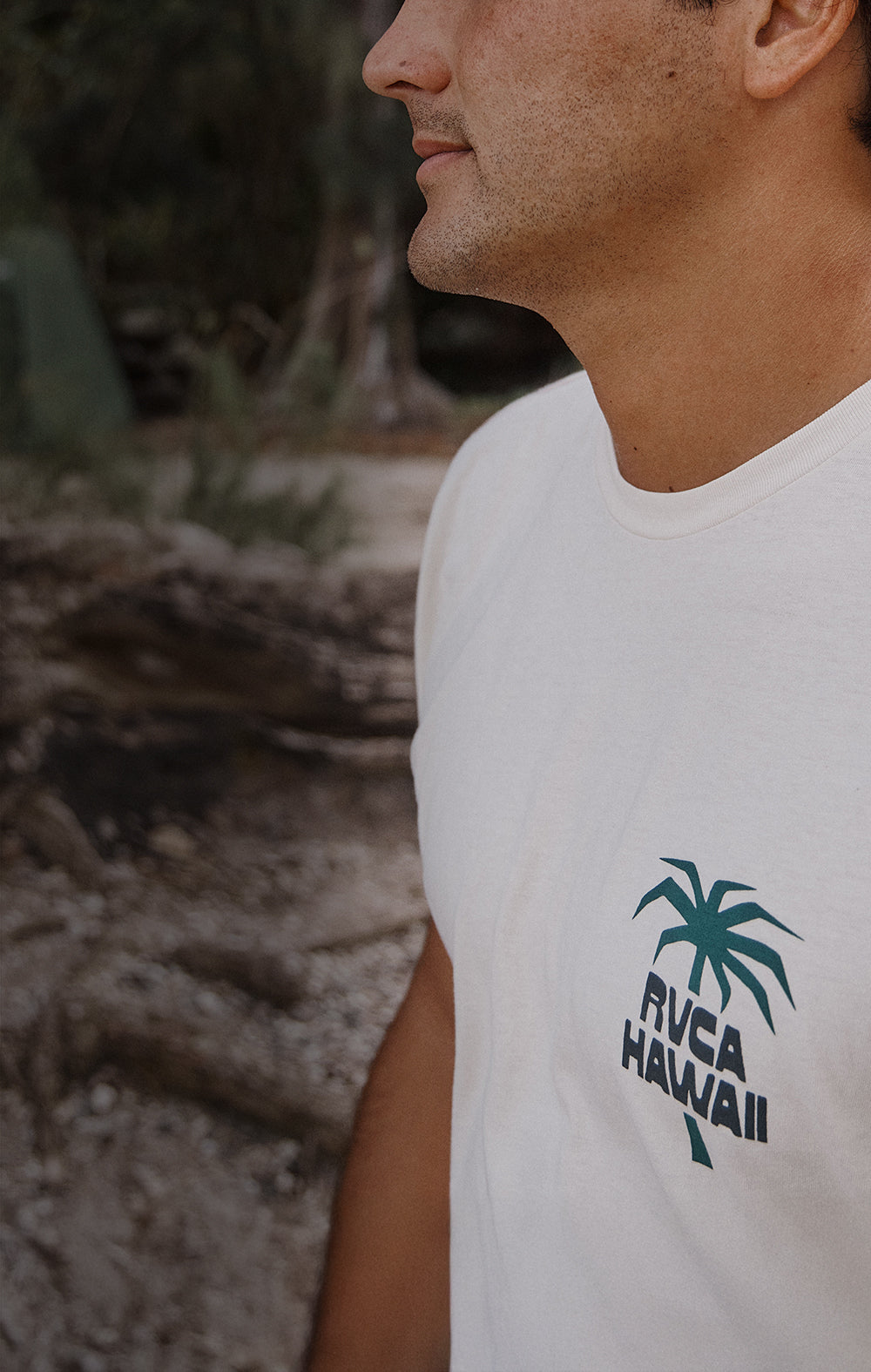 Person wearing a white sleeveless shirt with a palm tree design and 'RVCA Hawaii' text.