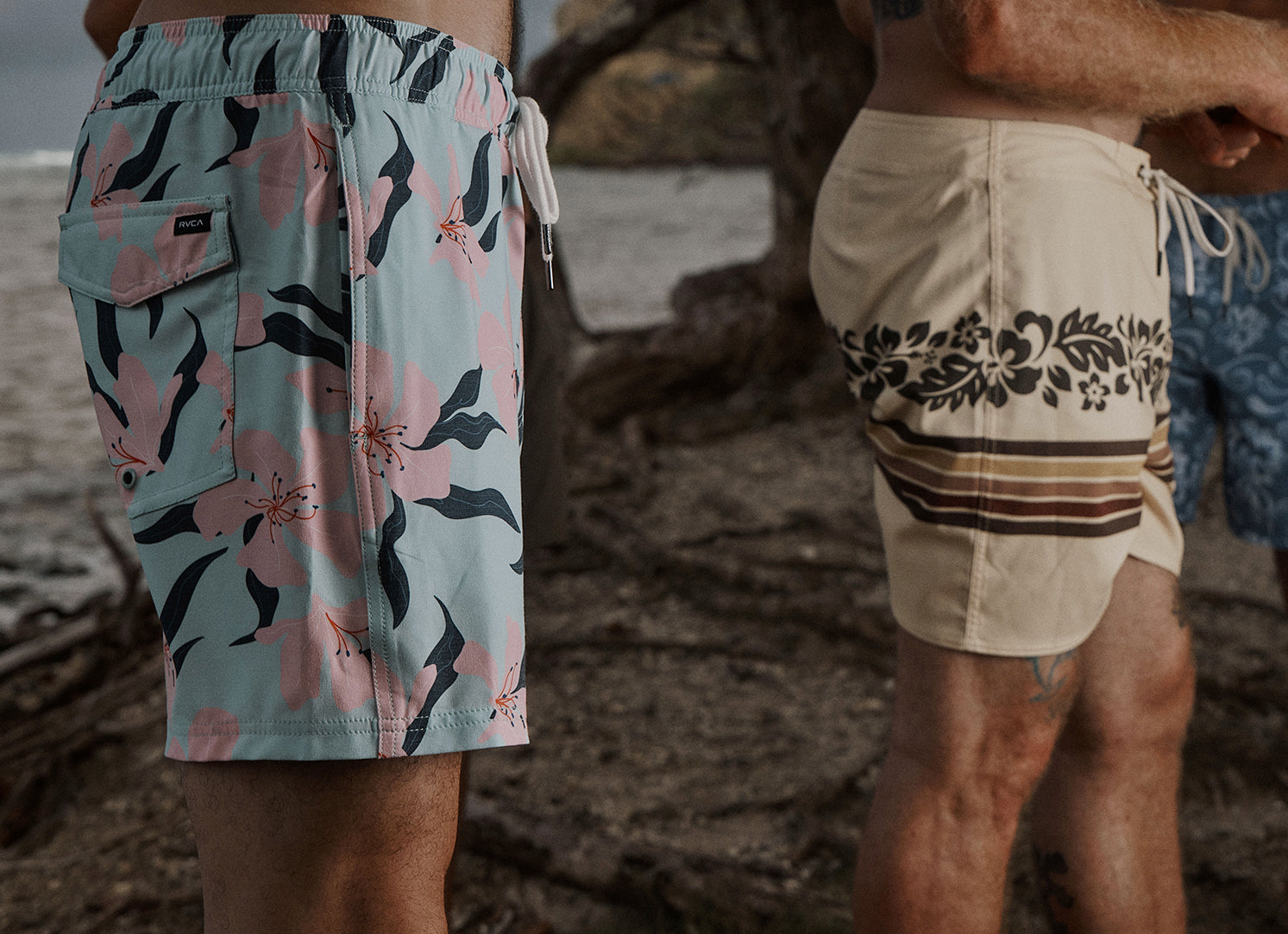 Two pairs of shorts, one with floral pattern and the other with a geometric design, on a beach setting.
