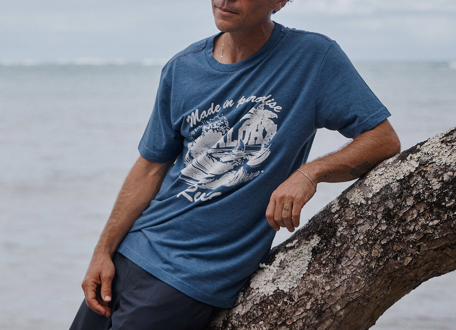 Man wearing a blue t-shirt with a graphic design, sitting by the ocean.