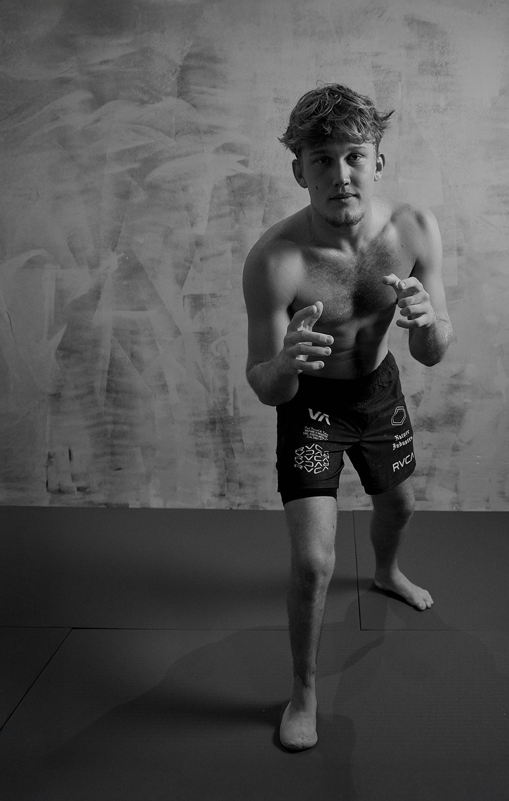 Man in athletic shorts posing against a textured wall.