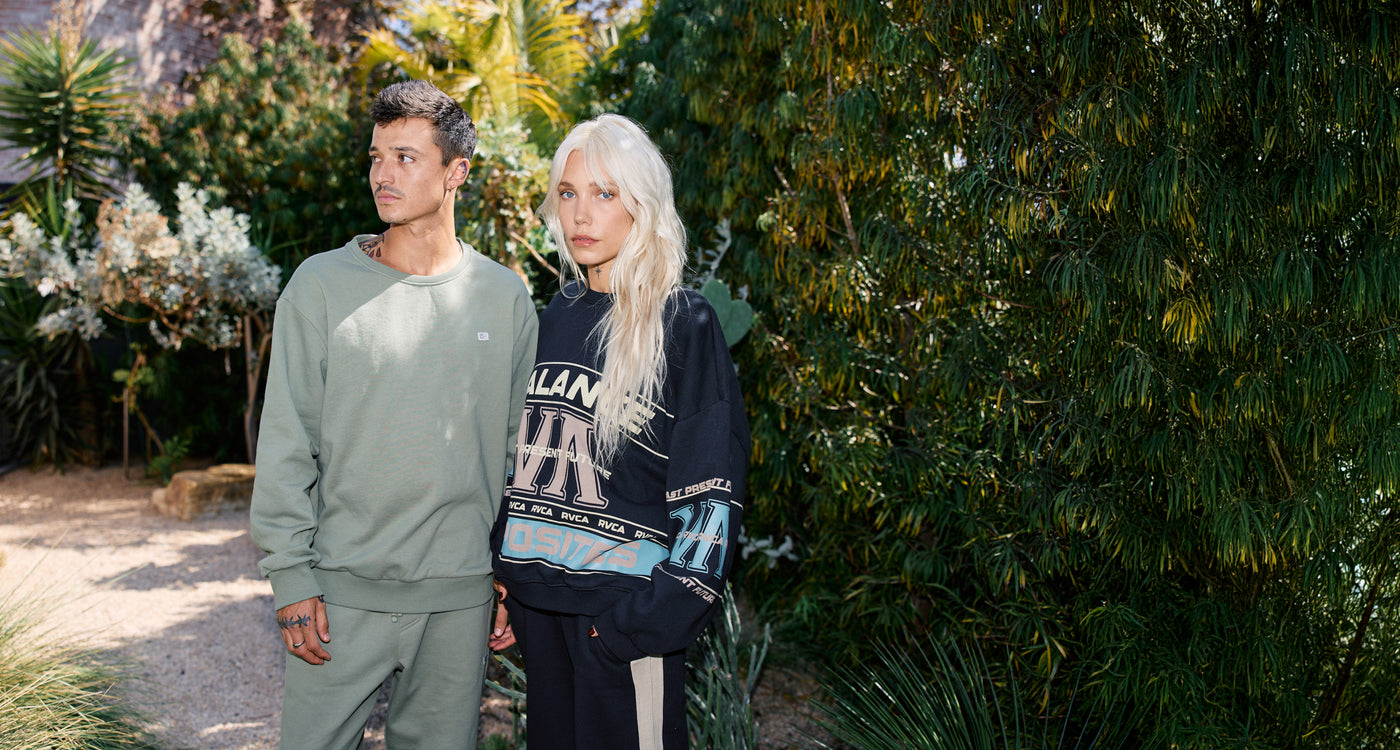 Two people standing outdoors with greenery in the background