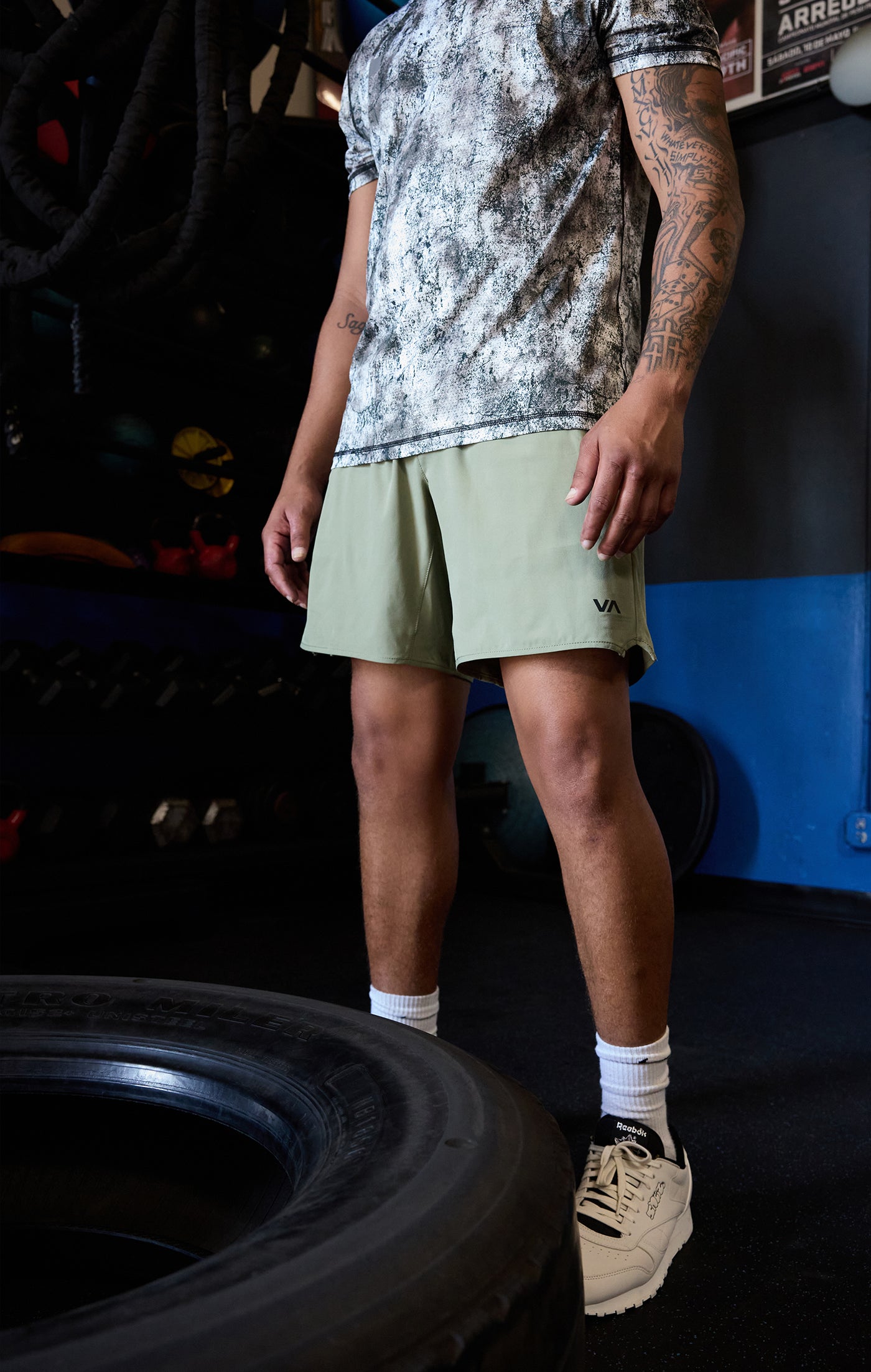 Person wearing a patterned shirt and light green shorts standing next to a tire indoors.