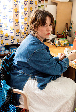 Woman sitting at a desk in a home office with colorful curtains in the background