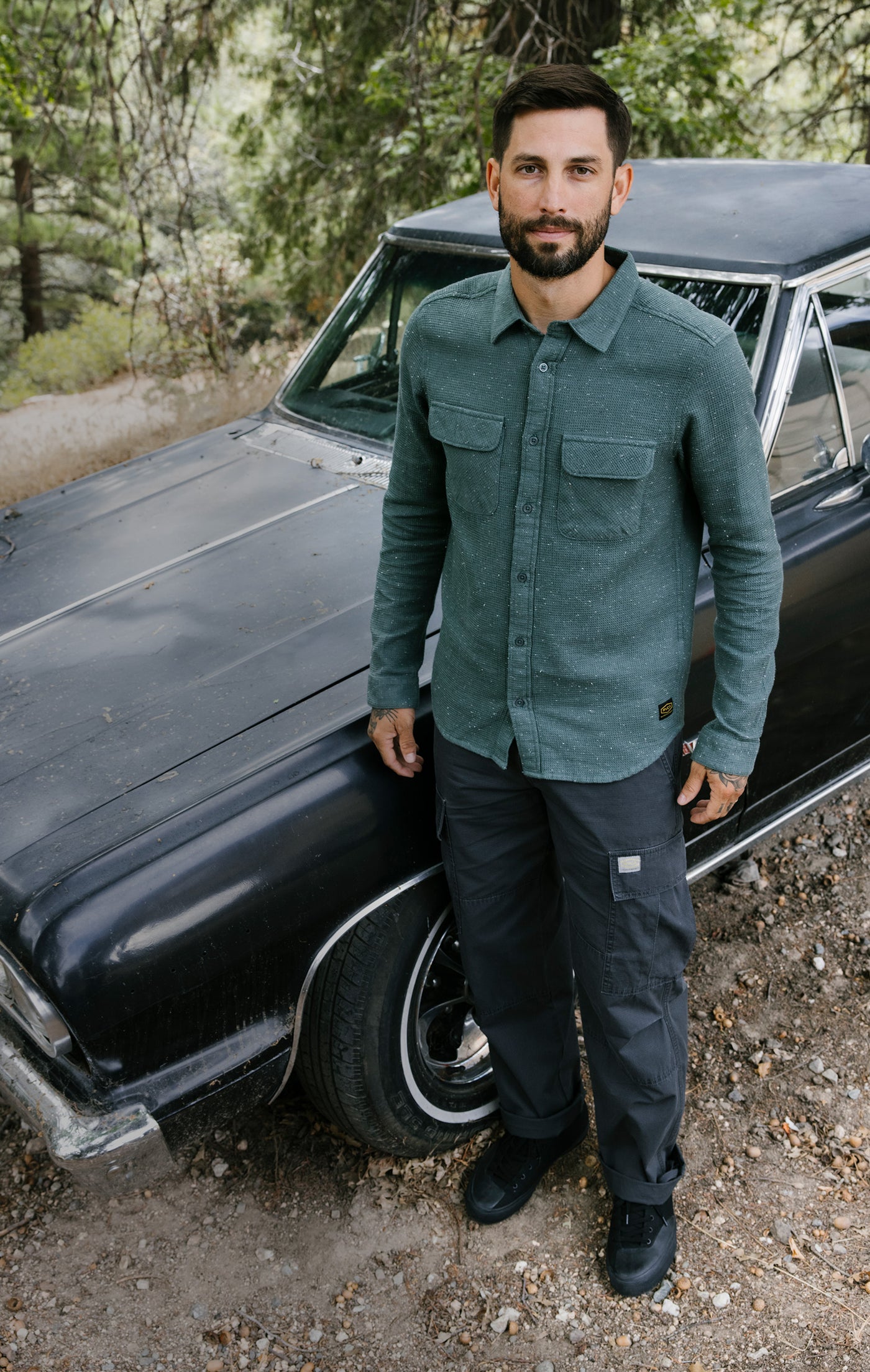 Man standing next to a vintage car in a forested area