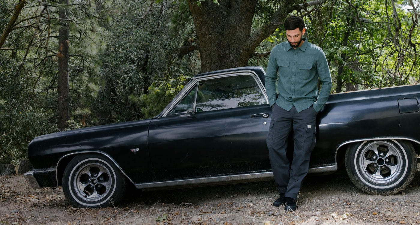 Man standing next to a classic black car in a forest setting