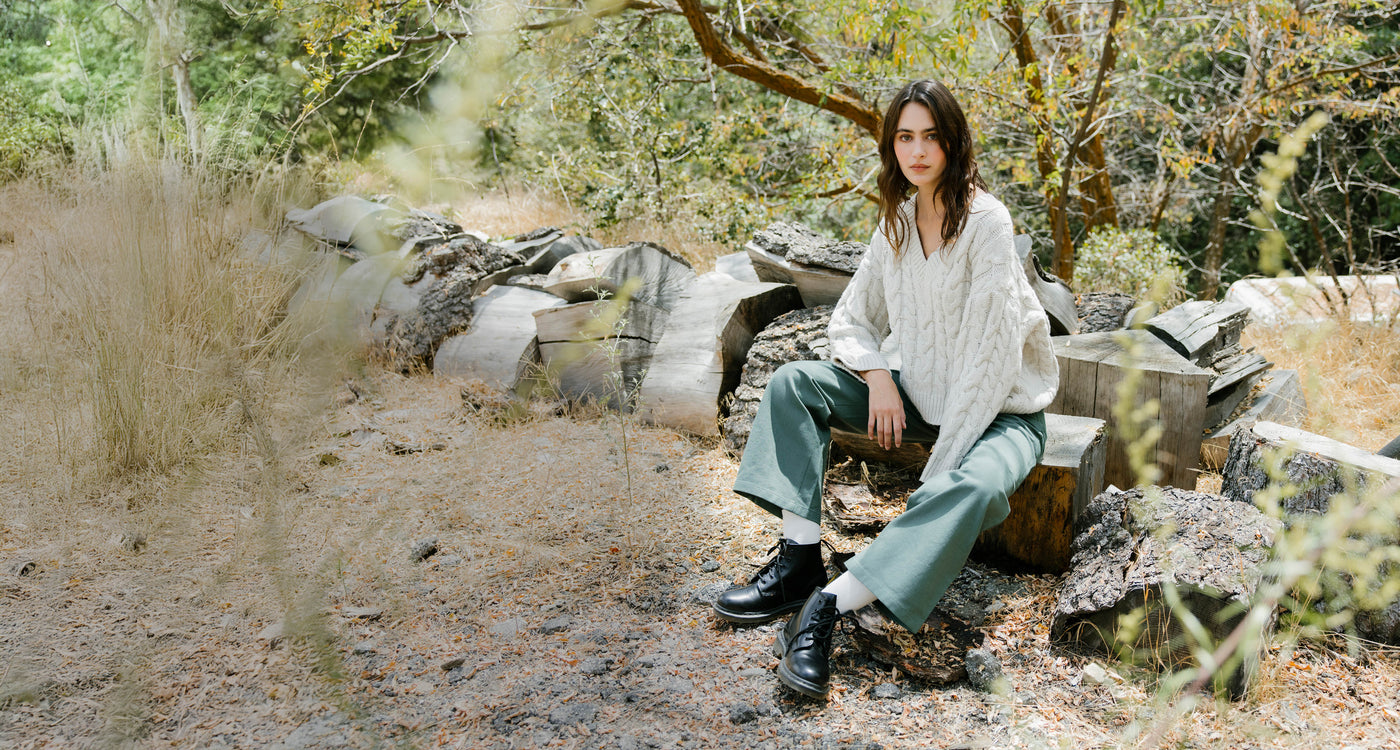 Person sitting on a log in a natural setting with trees and rocks.