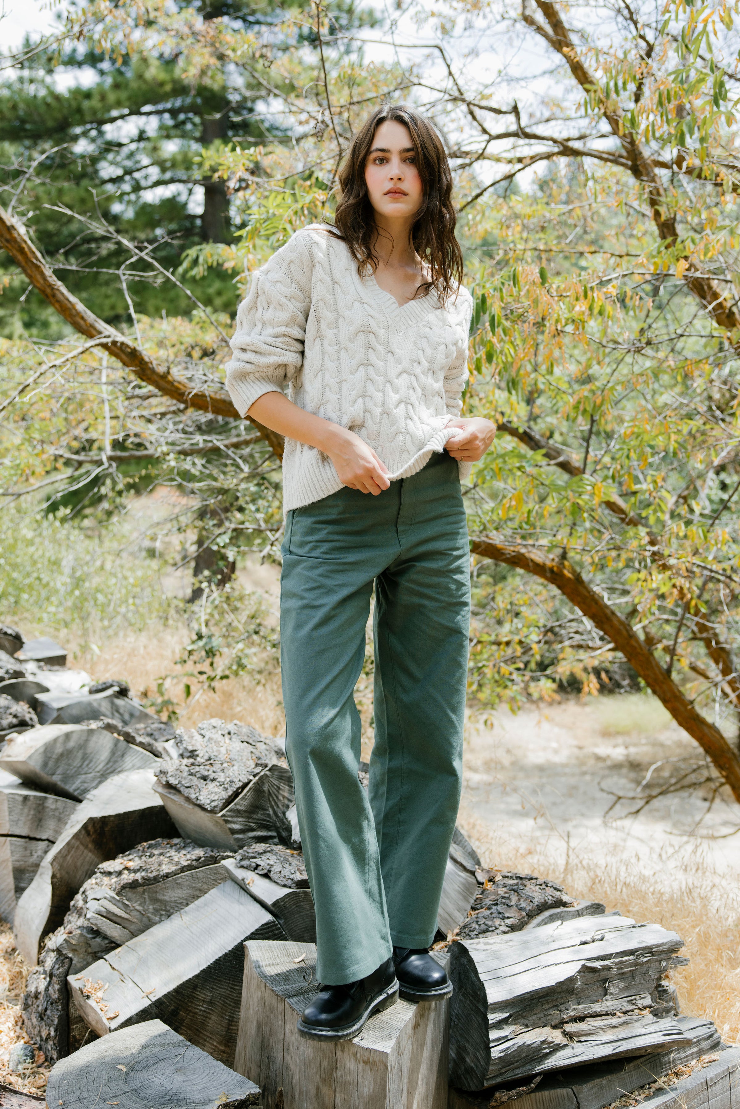Woman standing outdoors on a rocky surface with trees in the background