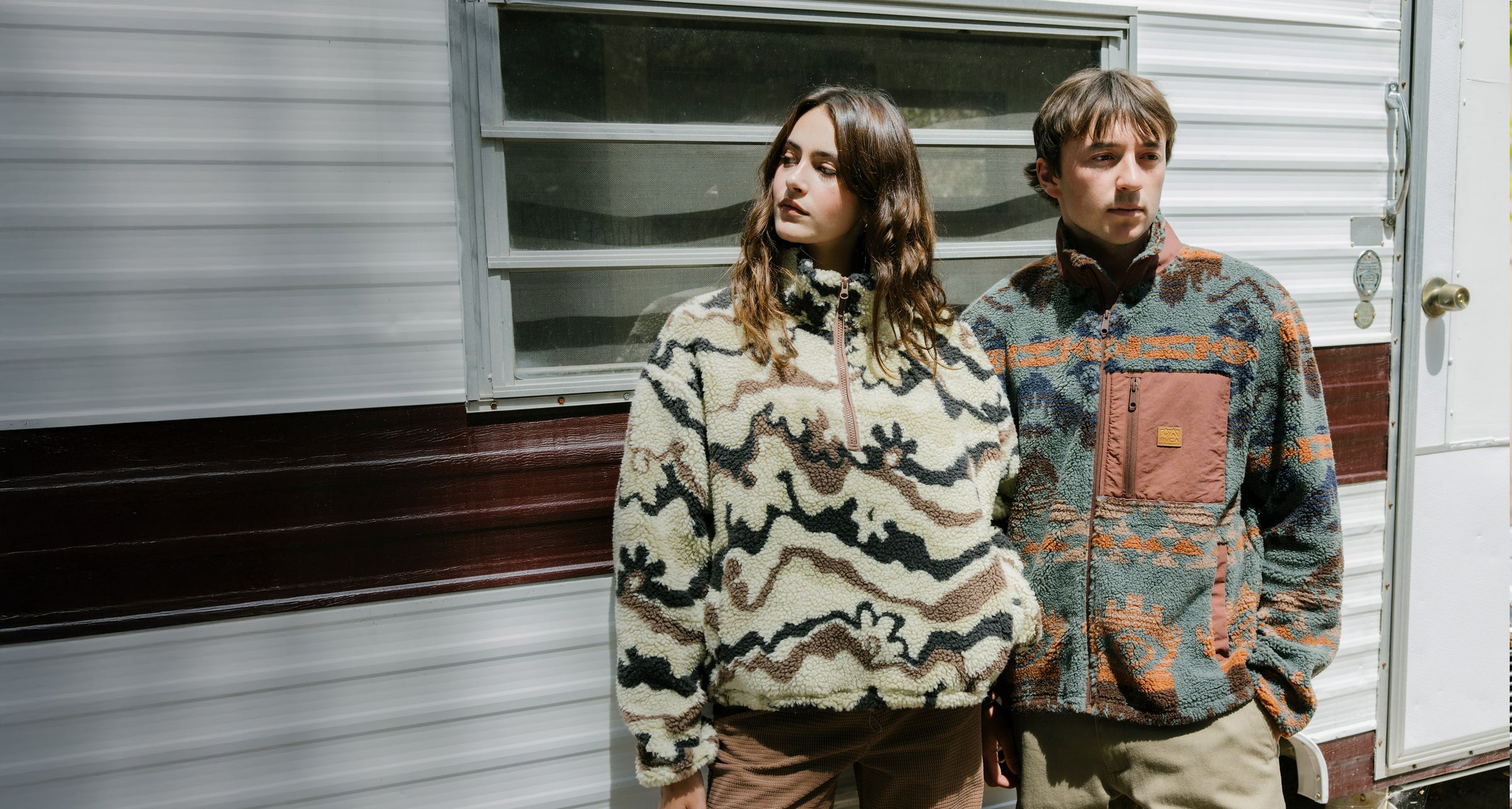 Two people standing in front of a trailer wearing patterned jackets.