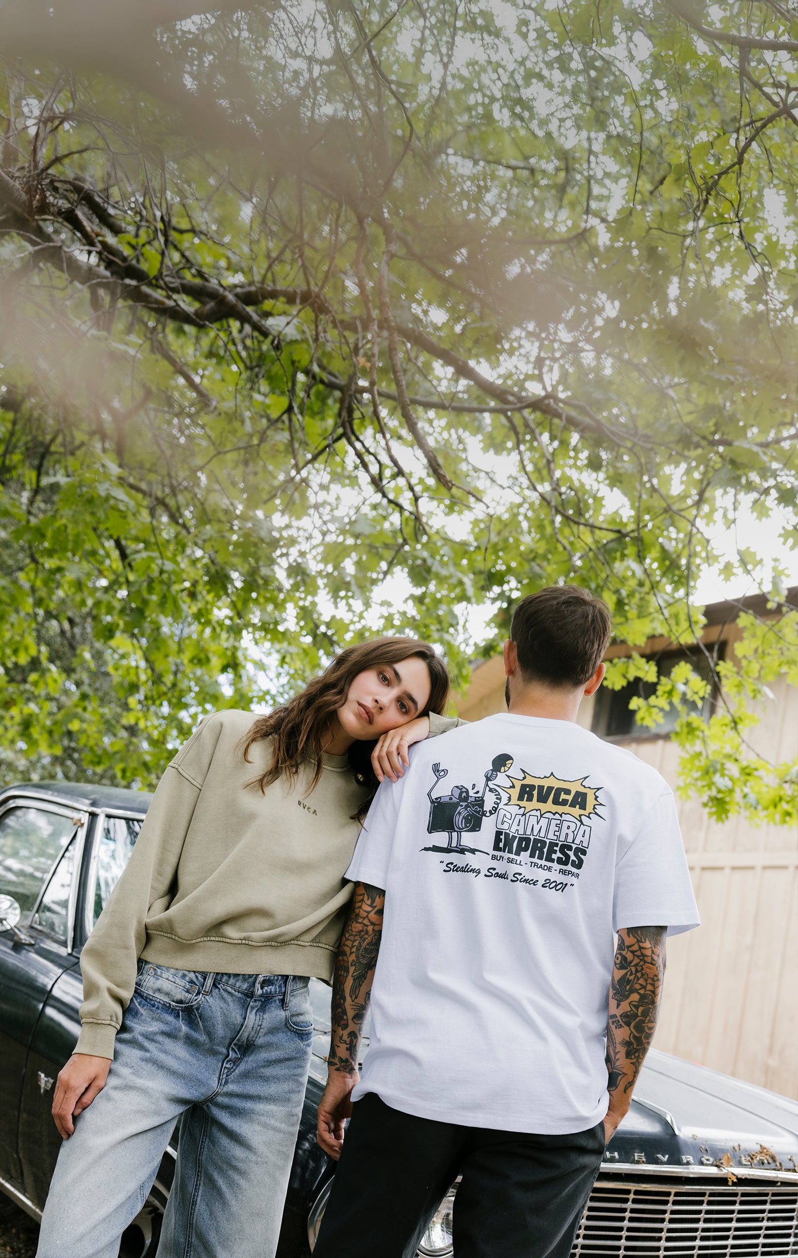 Two people standing close together with a car and trees in the background