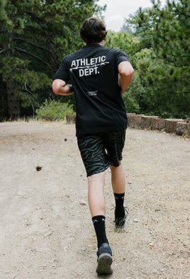 Person wearing an 'Athletic Dept.' t-shirt running on a dirt path with trees in the background.
