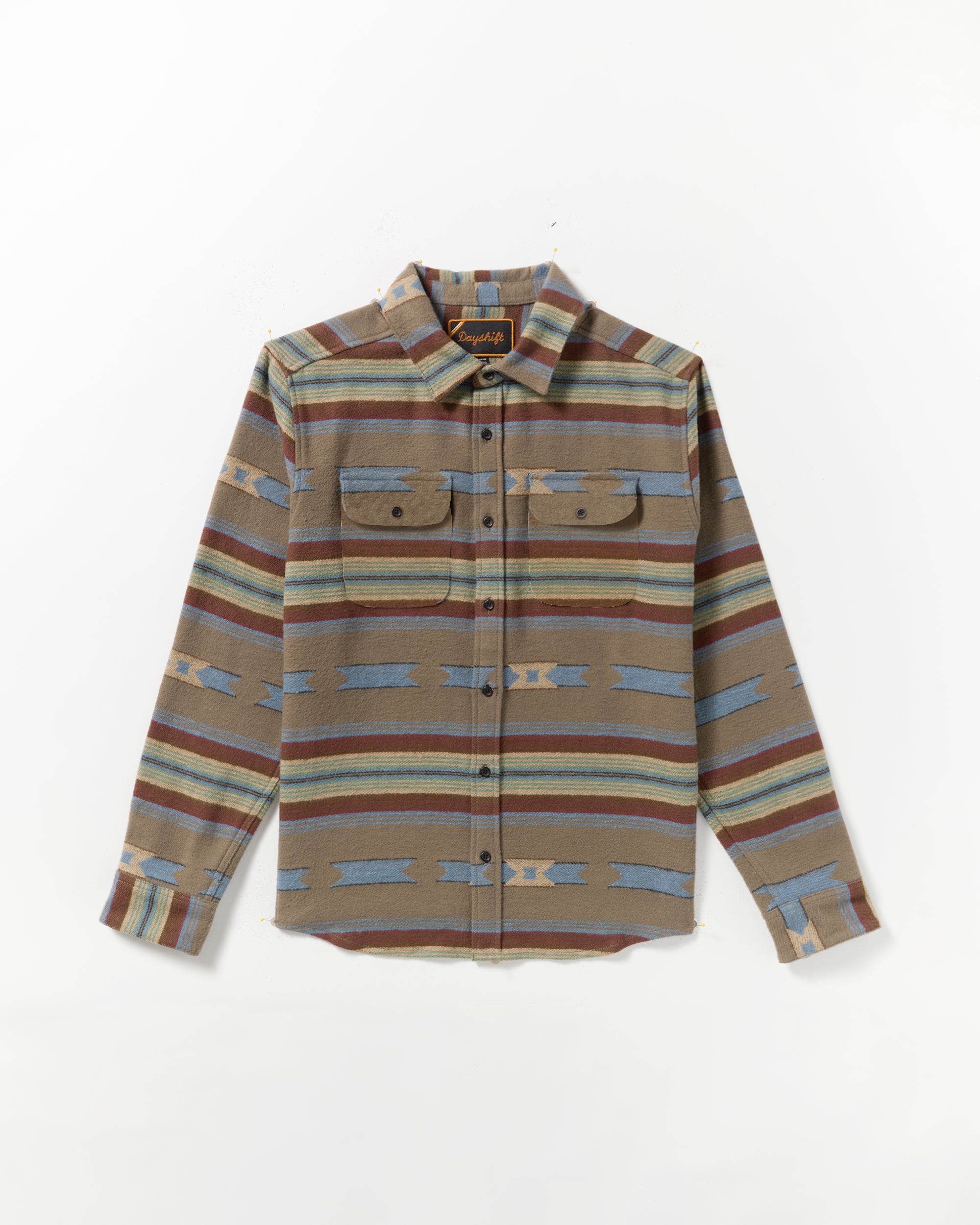 The Dayshift Blanket Flannel Long Sleeve Shirt features a southwestern-inspired pattern in brown, blue, and tan with two chest pockets, button flaps, and a pointed collar. Laid flat on a white background.