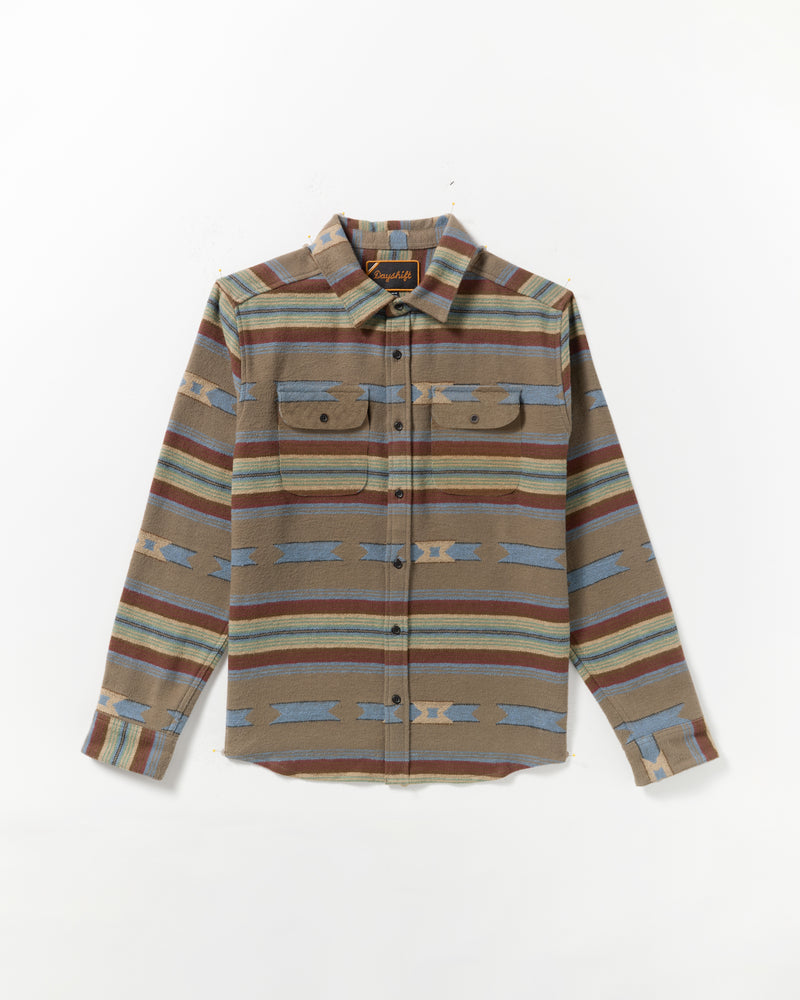 The Dayshift Blanket Flannel Long Sleeve Shirt features a southwestern-inspired pattern in brown, blue, and tan with two chest pockets, button flaps, and a pointed collar. Laid flat on a white background.