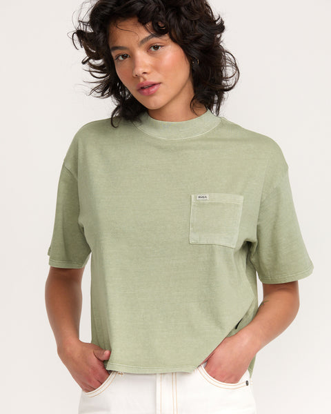 A person with wavy dark hair wears the Kinney Tee Pocket PTC in light green and off-white pants, standing against a plain light background.
