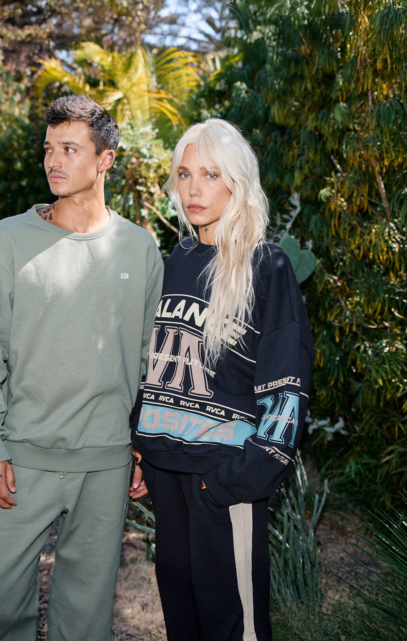 Two people standing outdoors with greenery in the background