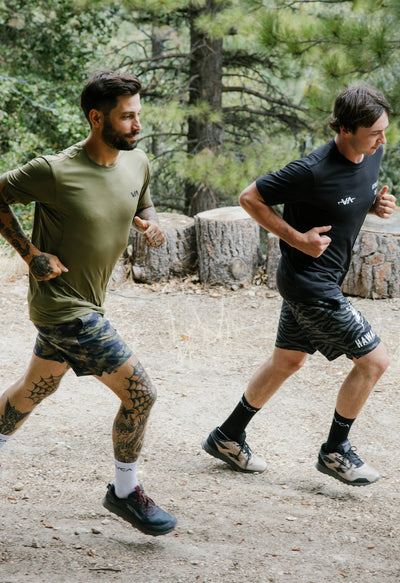 Two men running outdoors on a trail with trees in the background