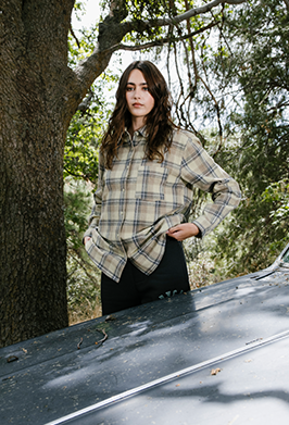 Woman in flannel standing in forest by a black car