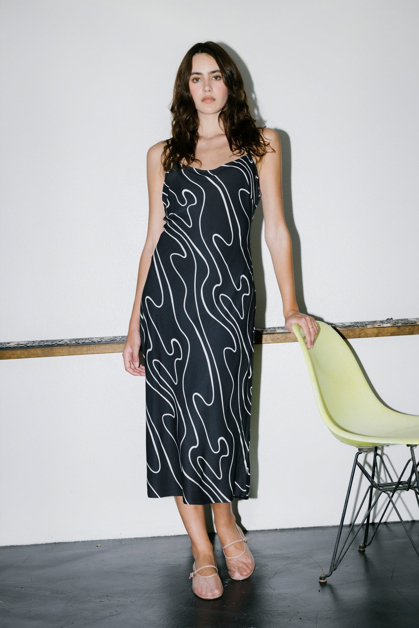 Woman wearing a black dress with white patterns in a minimalistic setting.